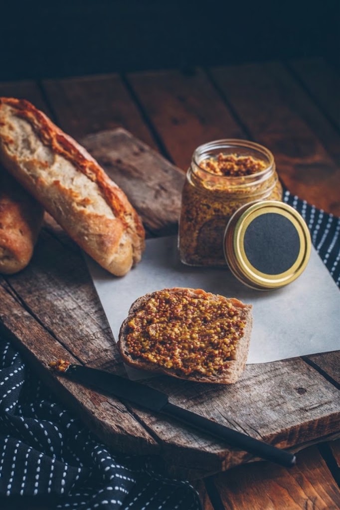 Mostaza en grano estilo artesanal en frasco de vidrio, untada sobre pan
